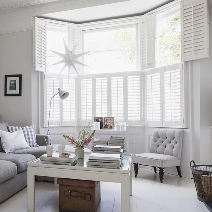 White polywood shutters in a bay window by a living room.