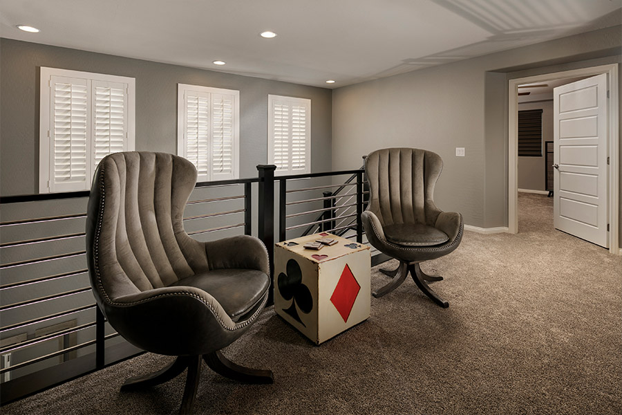 A white window treatment on a darker wall can do wonders for your Cincinnati home. two chairs and a small dice-themed table in front of a stairwell with shuttered covered small windows