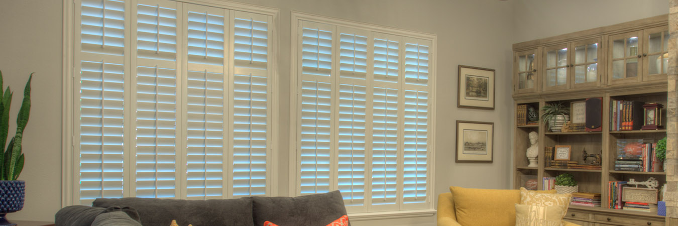 Large living room with white Polywood shutters next to a bookcase/tv.